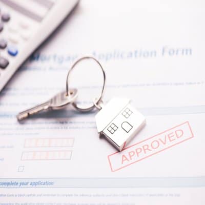 House shaped keychain resting on approved mortgage application form beside calculator, symbolizing successful home loan approval