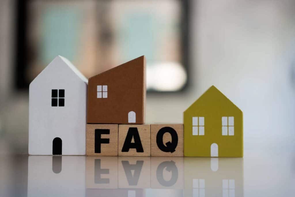 Small decorative house models placed on a surface with wooden blocks spelling FAQ in front
